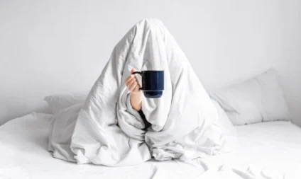 insonnia - Donna avvolta in una coperta seduta sul letto con una tazza di caffè tra le mani